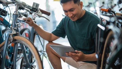 handsome young entrepreneur squatting to check a bicycle frame using a tablet handsome young entrepreneur squatting to check a bicycle frame using a tablet