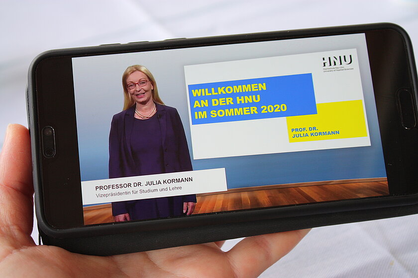 Smartsphone, auf dem das Begrüßungsvideo für Erstsemesterstudierende von Frau Prof. Dr. Julia Kormann gezeigt wird. (öffnet Vergrößerung des Bildes)