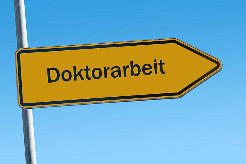 A yellow sign saying "doctoral thesis" against a blue sky (opens enlarged image)